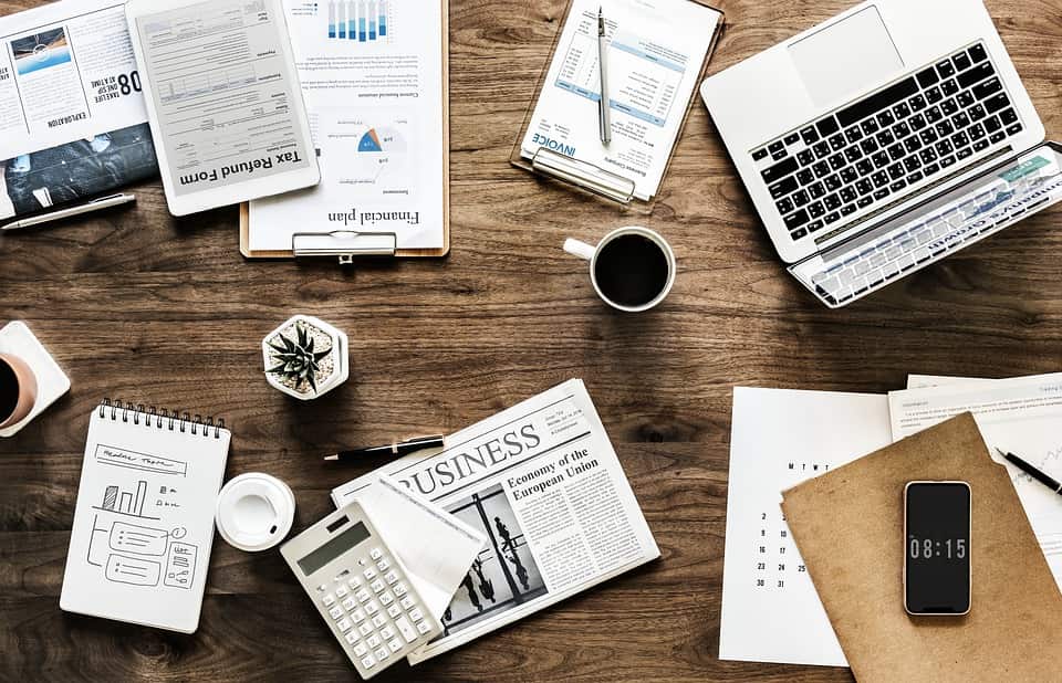 mesa com planilhas jornais calculadora um notebook e uma xicara de cafe