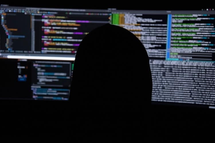 homem de capuz usando computadores com codigos de programacao