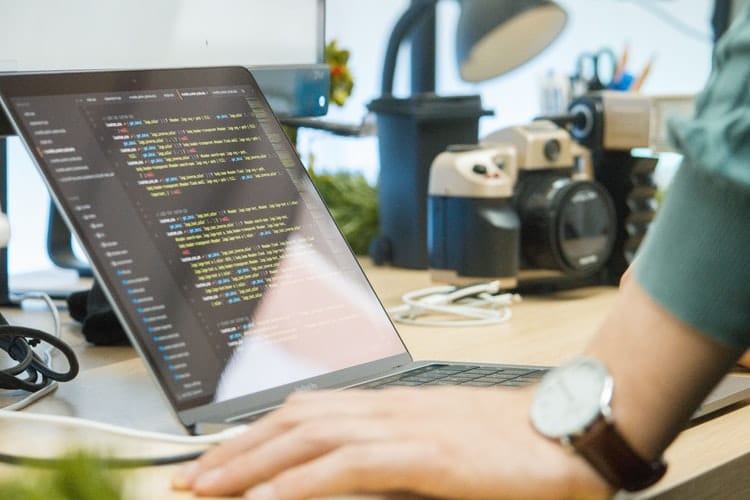 homem apoiado numa mesa com o notebook aberto com codigos de programacao