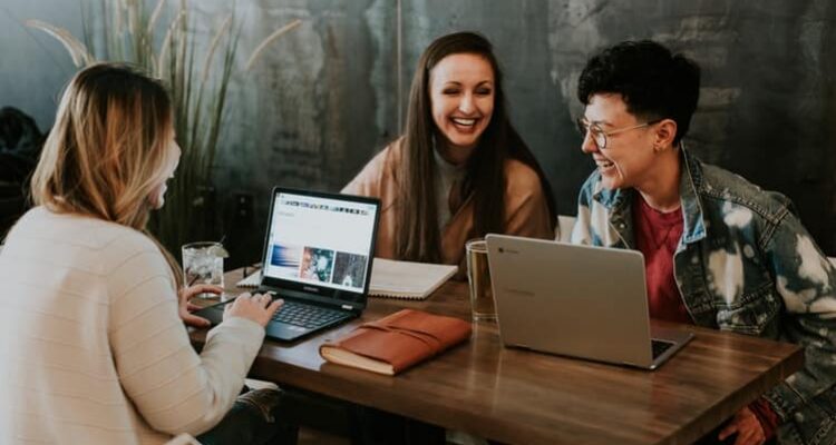 tres mulheres conversando e rindo perto de seus computadores