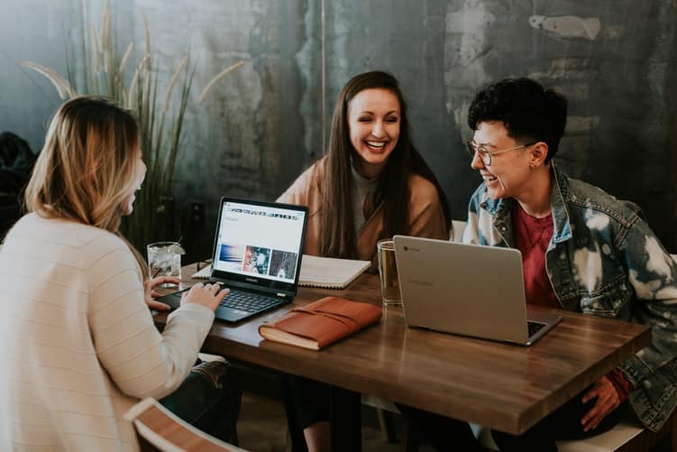 tres mulheres conversando e rindo perto de seus computadores