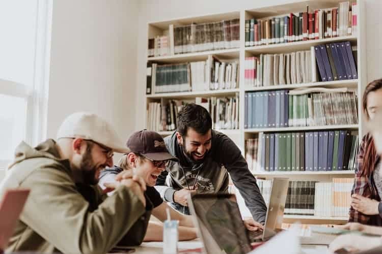 tres homens olhando juntos para um notebook e rindo