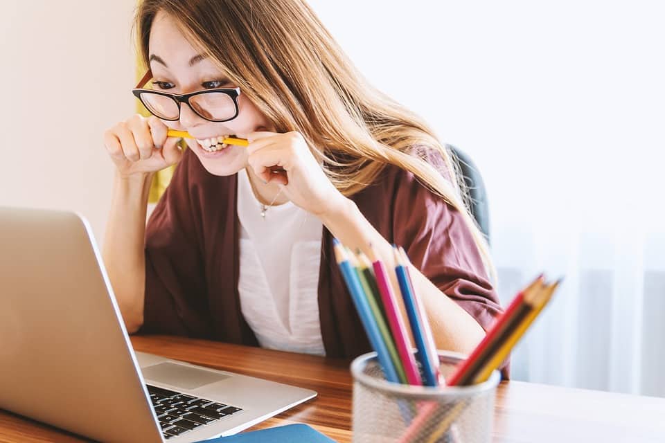 mulher mordendo um lapis e olhando o computador