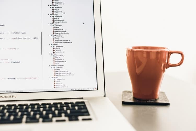 imagem de tela de computador com codigos de programacao HTML com xicara de cafe ao lado
