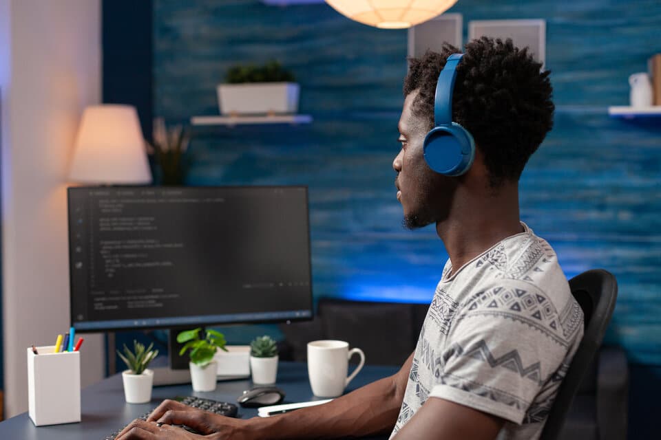 Homem sentado em frente à uma mesa trabalhando em seu computador.