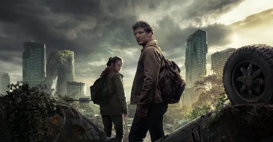 Joel e Ellie, personagens de The Last of Us, caminham entre veículos abandonados em uma cidade tomada pela vegetação, com prédios em ruínas ao fundo e um céu nublado.